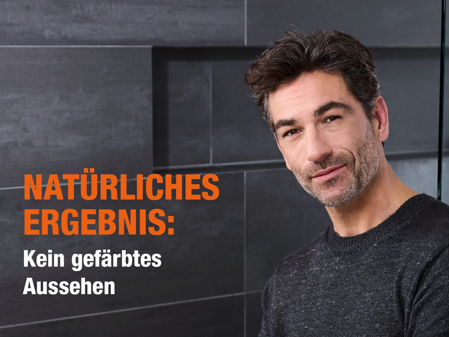 Ein Mann mittleren Alters mit dunklem, leicht ergrautem Haar und Dreitagebart, der in die Kamera lächelt. Im Hintergrund eine dunkle Badezimmerwand. Text in großen, orange-weißen Buchstaben: ‚SCHNELL SICHTBAR: Dunklere Haare nach nur 2 Wochen bei täglicher Anwendung‘ und ‚NATÜRLICHES ERGEBNIS: Kein gefärbtes Aussehen‘